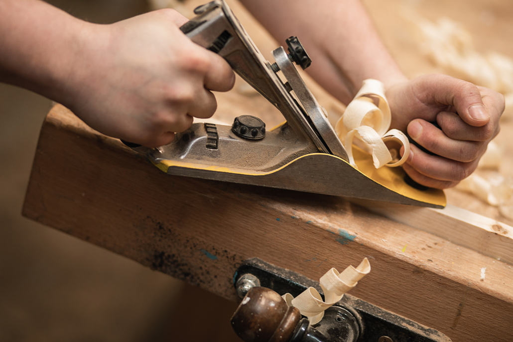 Block plane being used to remove a thin layer of wood.