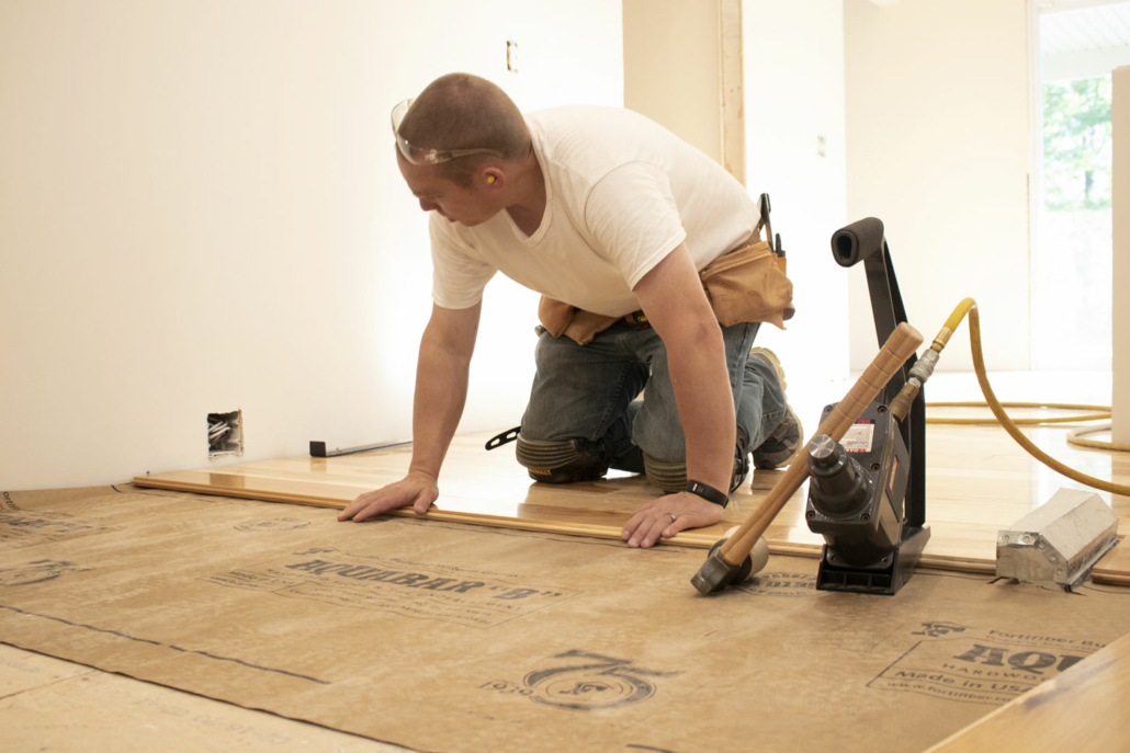 A man installing tongue and groove hardwood flooring. 