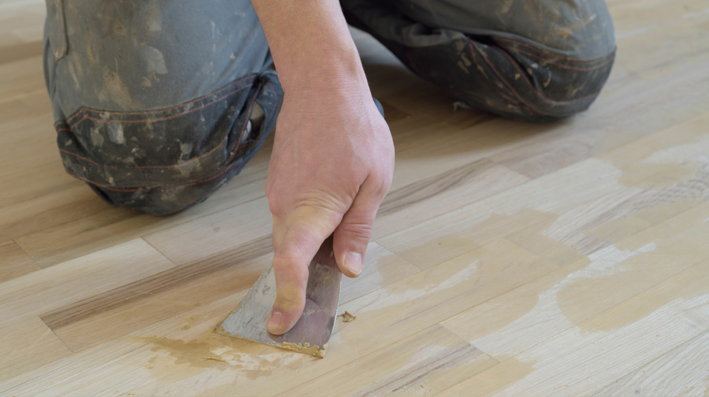 A man filling nail holes with putty after installing hardwood floors.